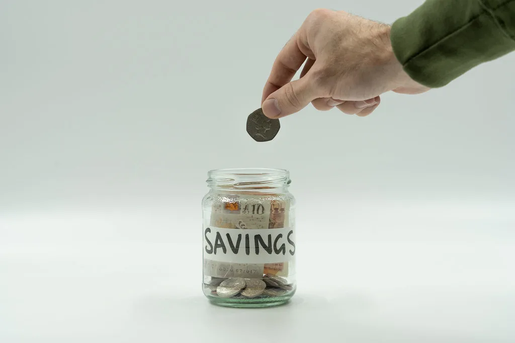 Coins saved in a glass jar — Emergency Fund 2026: How to Build $1,000 Fast on Any Income